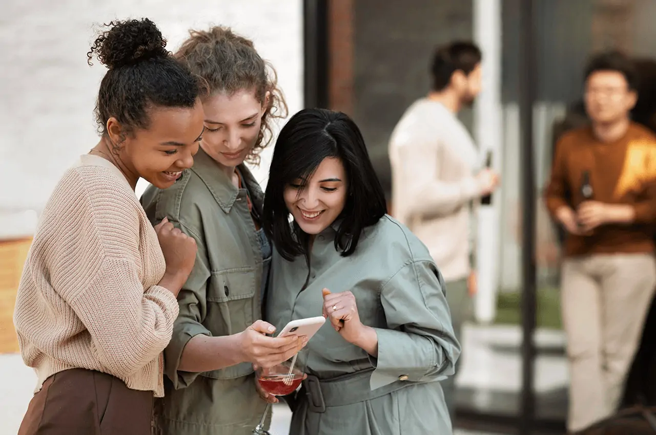 três mulheres olhando para o celular em um evento