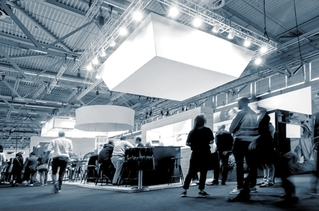 pessoas caminhando entre estandes em um espaço de exposições corporativa