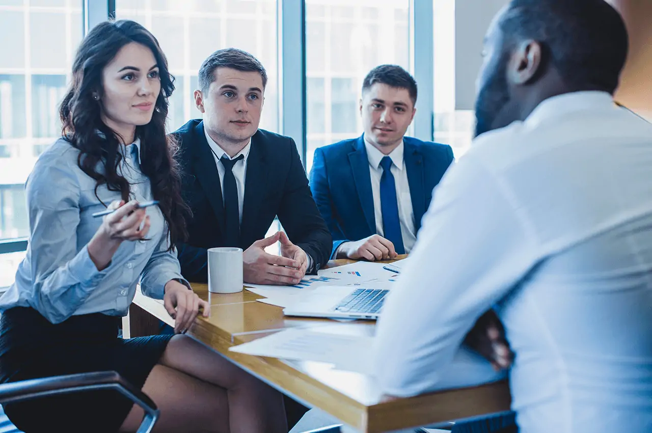 pessoas sentadas em uma reunião com papéis e notebook sobre a mesa