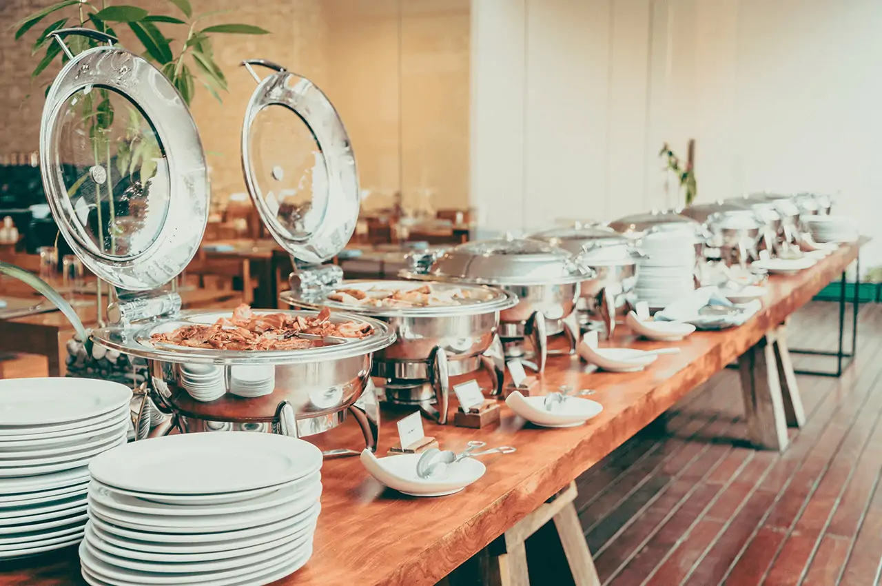 buffet com vários rechaud e pratos brancos em cima da mesa