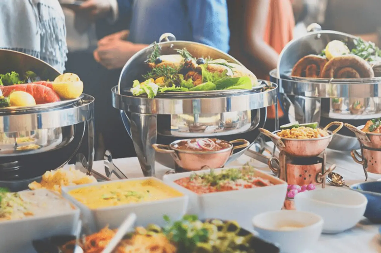 mesa de buffet com rechaud e recipientes brancos em cima da mesa