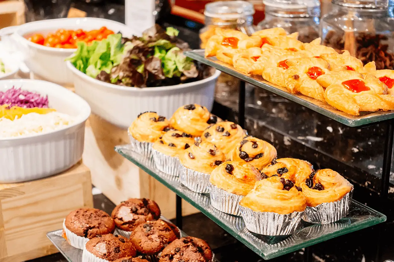 buffet com pequenos bolos, doces e saladas em um recipiente branco