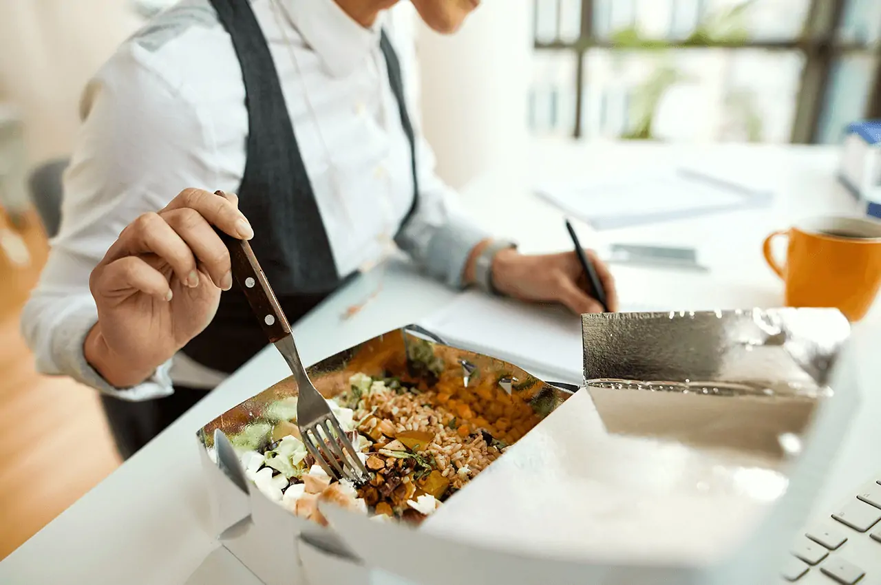 pessoa sentada na cadeira de escritório, comendo em um box brunch