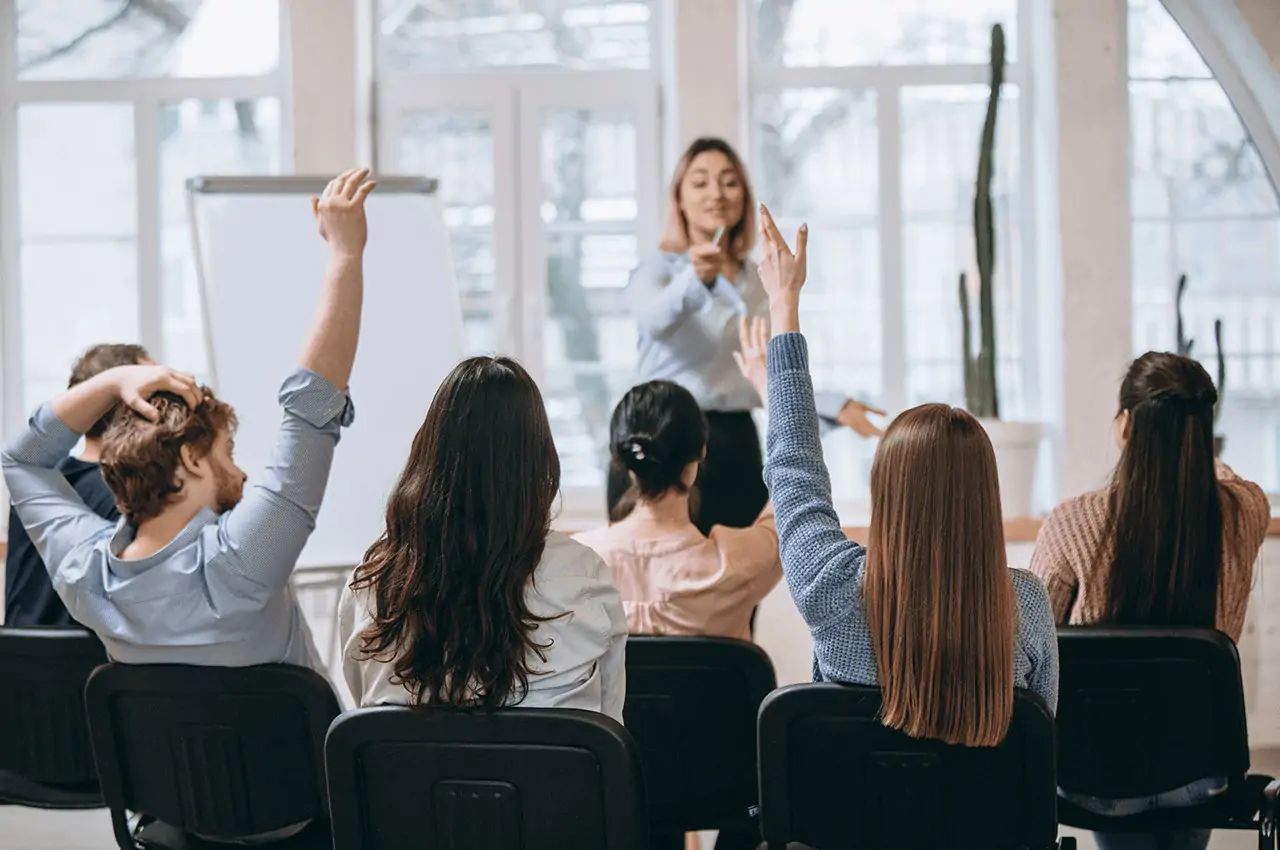 pessoas sentadas e outras com a mãos estendidas em um treinamento corporativo