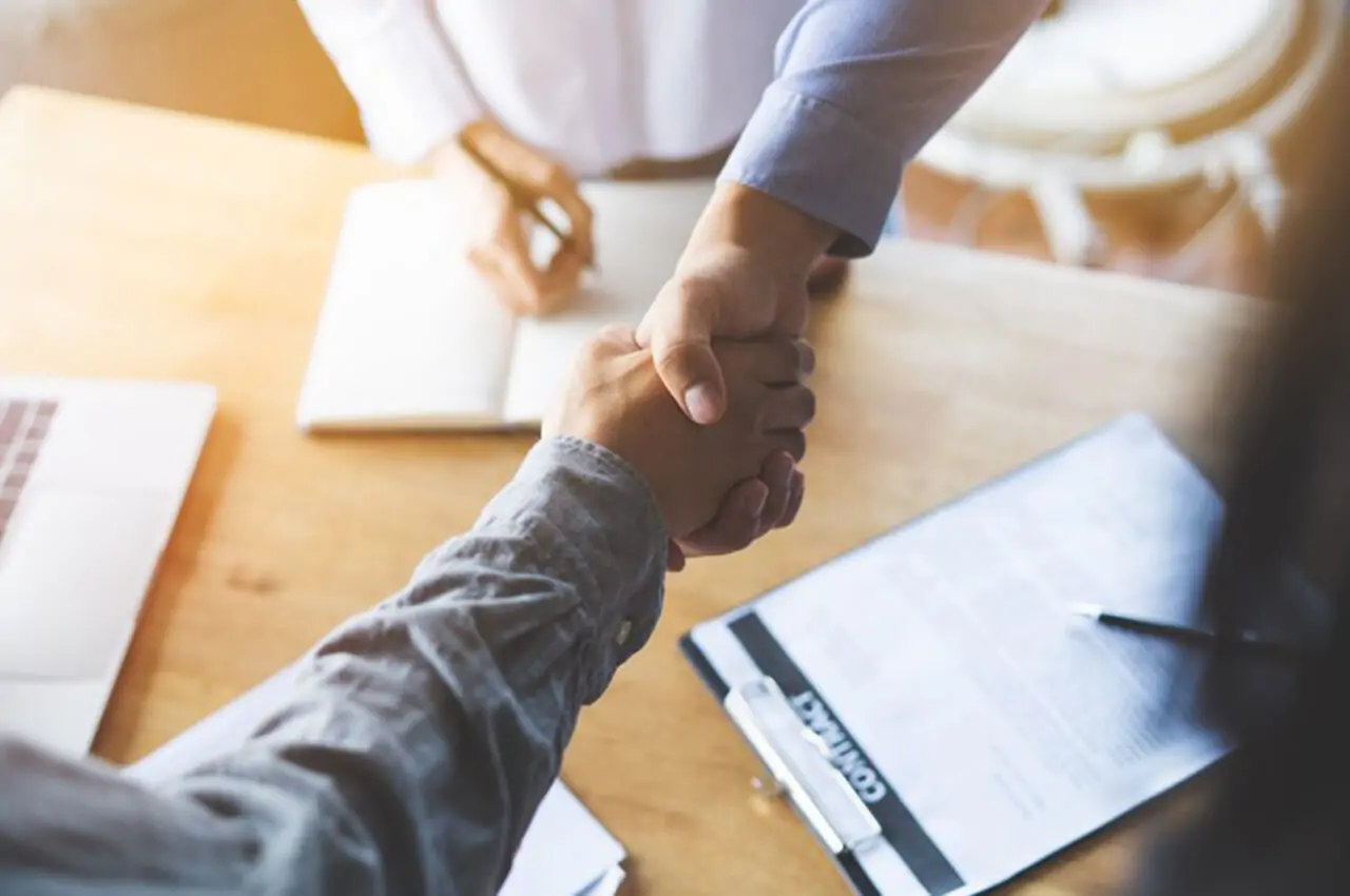 duas pessoas dando as mãos e na mesa abaixo o contrato para evento corporativo