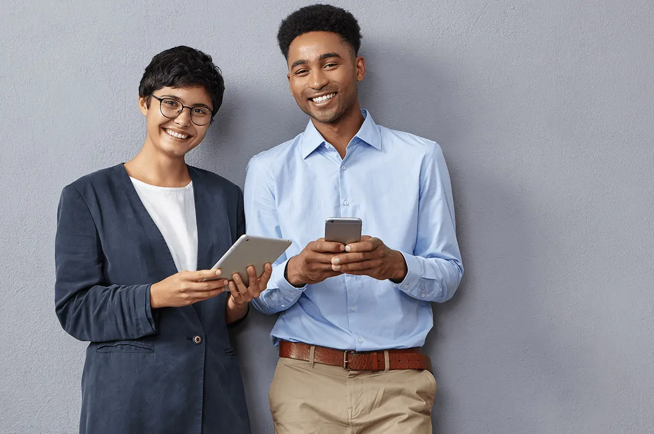 duas pessoas sorridentes segurando tablet e celular nas mãos