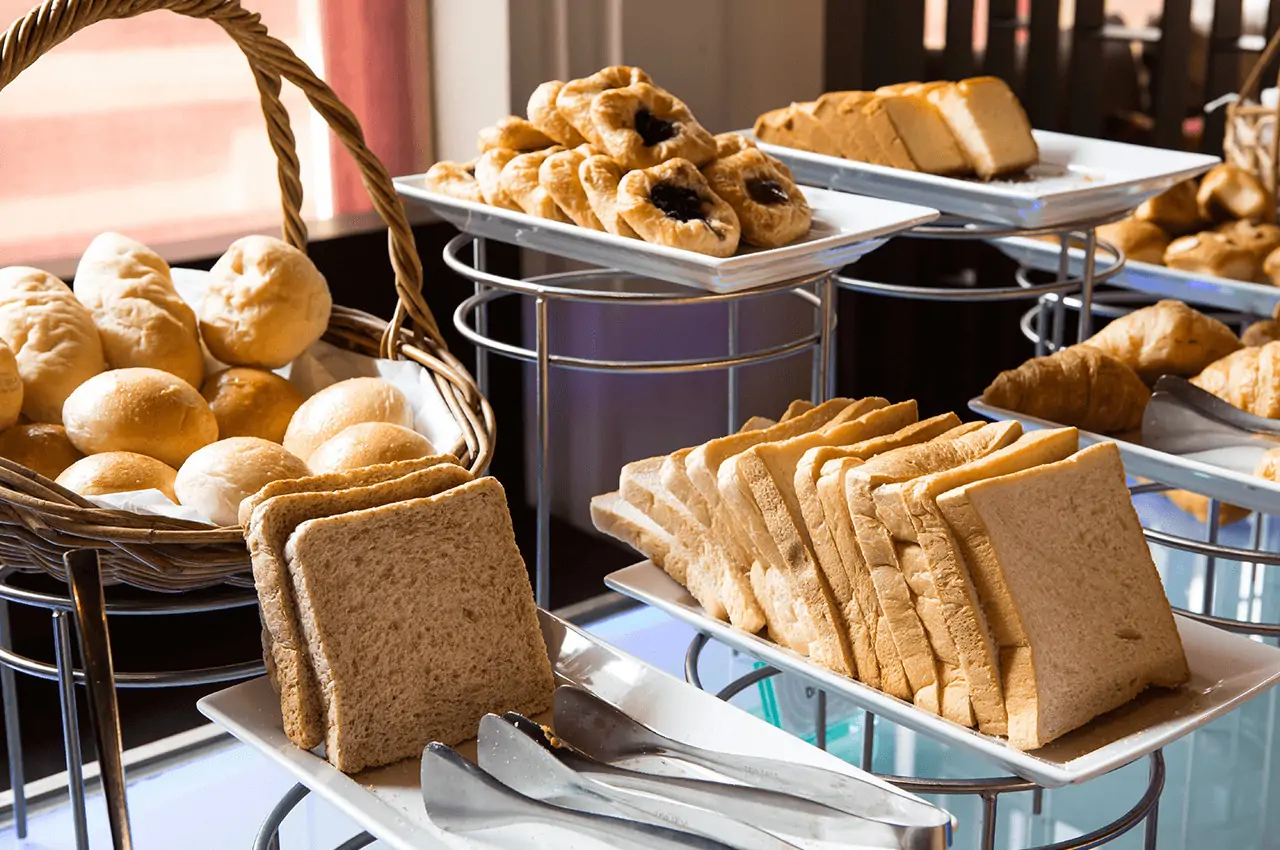 buffet com cesta de pães, croissants e bolos em cima de pratos brancos